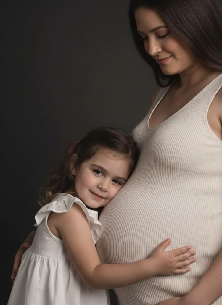 ИИ-фотосессия по фото: беременная мама в светлом трикотажном платье и маленькая дочь в белом сарафане, обнимающая мамин живот на темном студийном фоне.